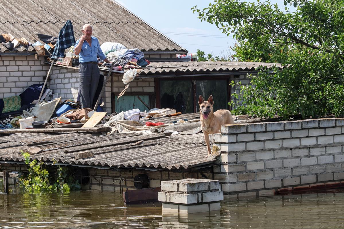 A man stands and his roof with his dog as the floodwaters from the collapse of the Kakhovka dam continue to rise in Ukraine’s Kherson region, 9 June 2023. Photo: EPA-EFE/MYKOLA TYMCHENKO