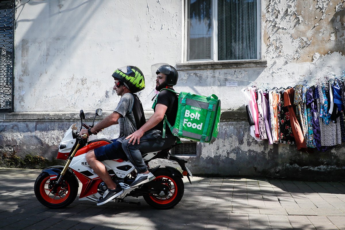 Доставщики еды проезжают мимо выставленной на продажу одежды на одной из улиц Батуми, 06 июля 2023 года. Фото: Юрий Кочетков / EPA-EFE