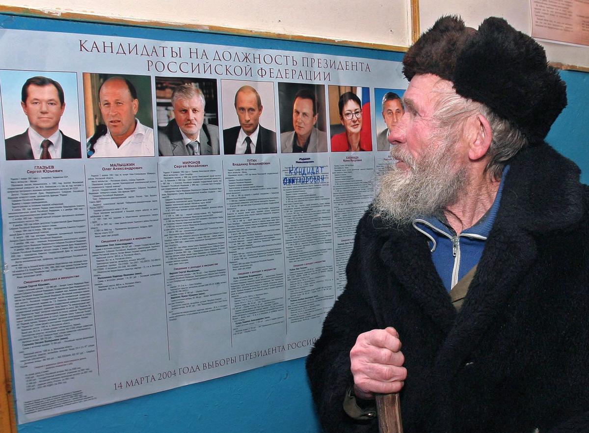 74-летний Дмитрий Баиндин смотрит на плакаты с кандидатами в президенты, входя на избирательный участок для досрочного голосования в деревне Ключевой Кемеровской области, Западная Сибирь, суббота, 13 марта 2004 года. Фото: Рашид Саликхов / EPA
