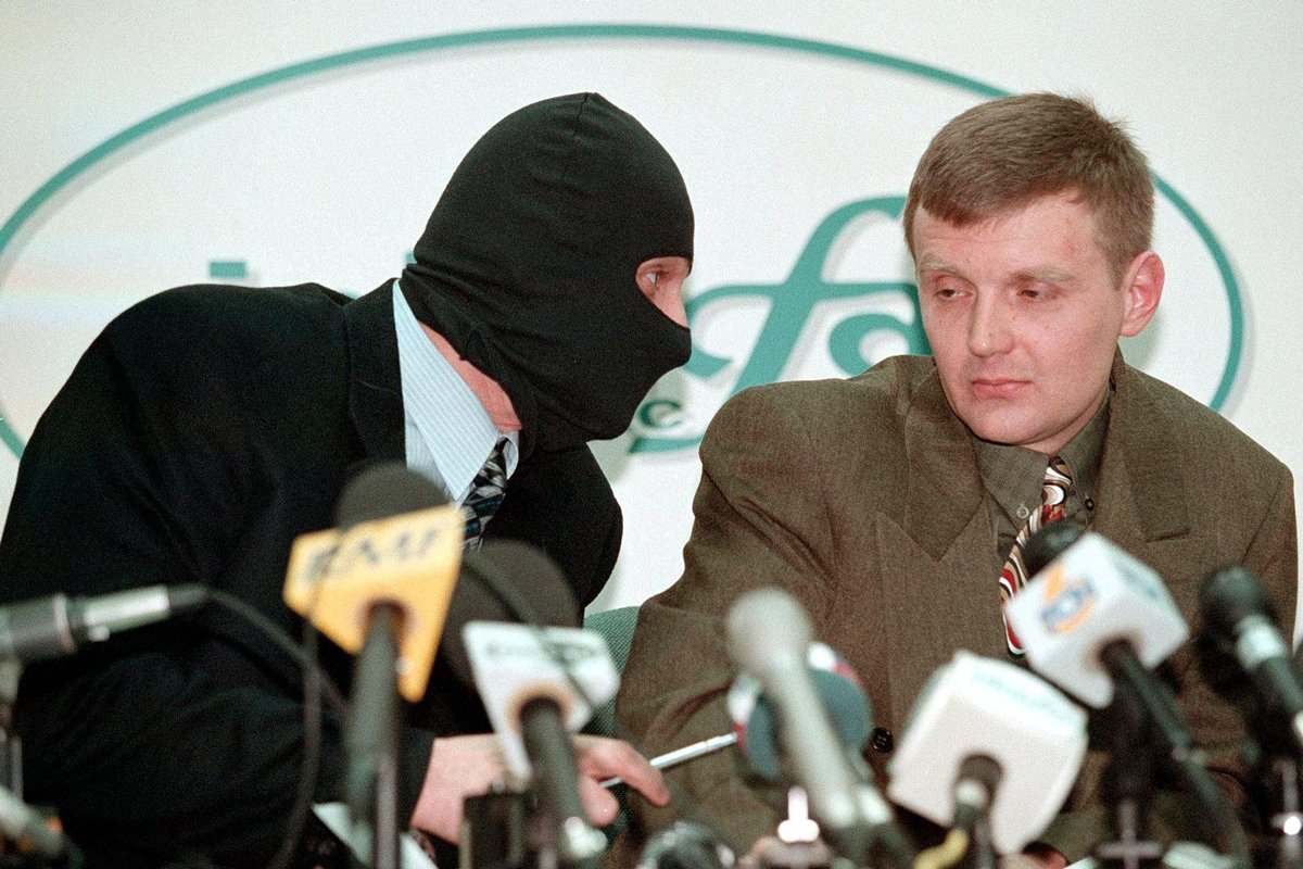 Александр Литвиненко и его коллега в маске для защиты личности разговаривают друг с другом во время пресс-конференции в информационном агентстве «Интерфакс», 17 ноября 1998 года. Фото: Сергей Каптилкин / EPA