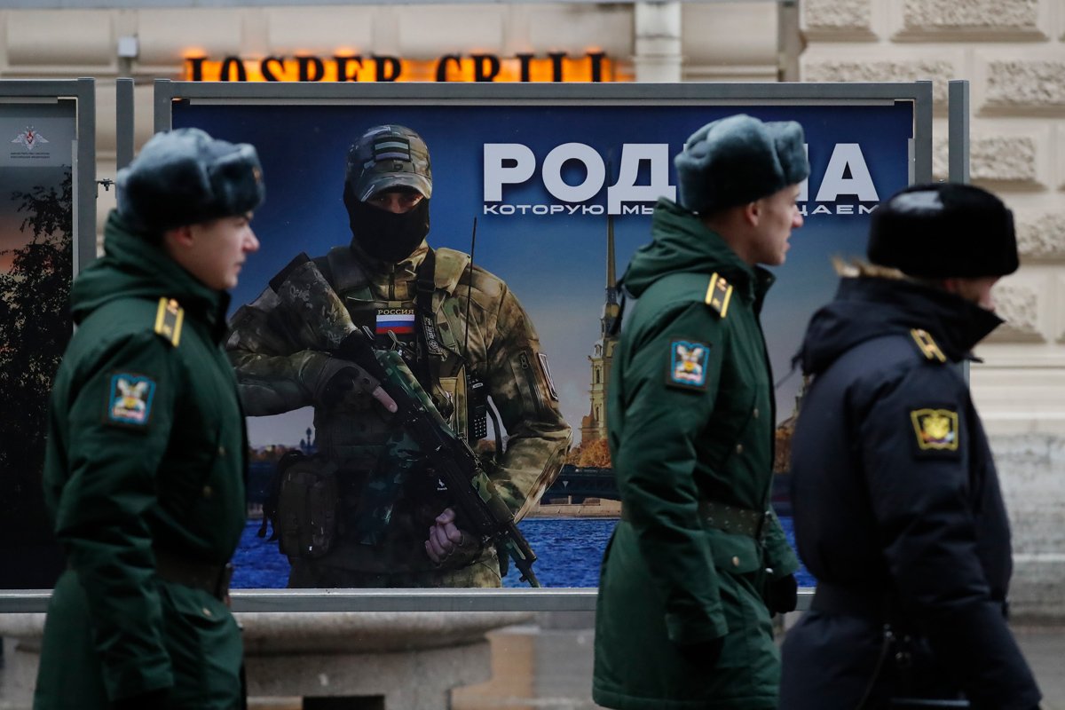 Военный патруль проходит мимо плаката с изображением российского военнослужащего и словами «Родину защищаем» в Санкт-Петербурге, 17 февраля 2023 года. Фото: Анатолий Мальцев / EPA-EFE