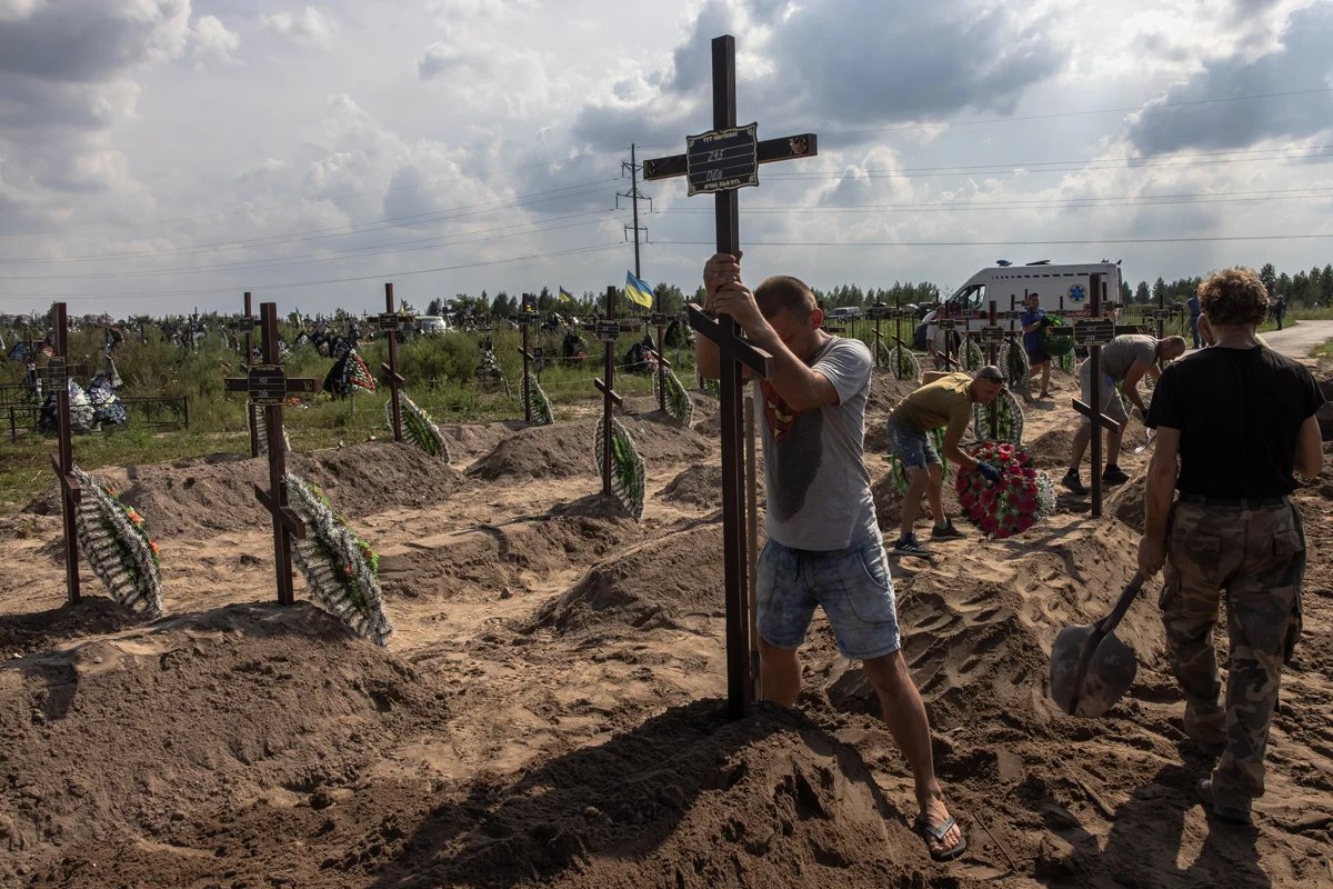 A man places a cross on the grave of an unidentified man killed during the Russian occupation of Bucha, August 2022. Photo: Roman Pilipey / EPA-EFE