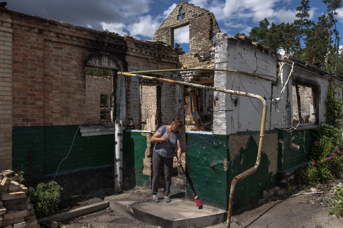 Жительница села Мощун, находящегося недалеко от Бучи и Ирпени, очищает от обломков территорию вокруг своего дома, разрушенного во время российских атак, 18 июля 2022 года. Фото: Роман Пилипей / EPA-EFE