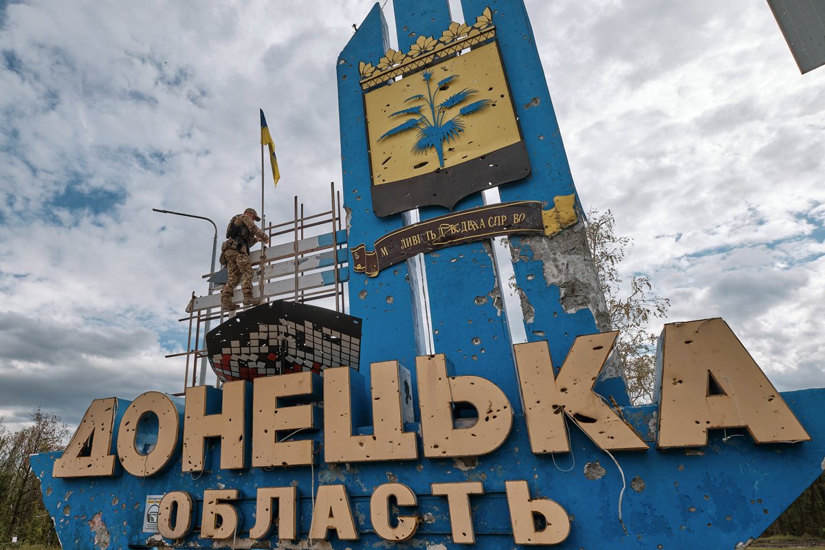Военнослужащий поднимает украинский флаг над стелой на въезде в Донецкую область, Украина, 20 сентября 2022 года. Фото: Евгений Гончаренко / EPA-EFE