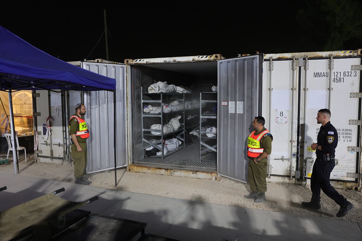 Израильские солдаты и полицейские открывают рефрижераторный контейнер с телами жертв теракта, совершенного ХАМАС 07 октября, в ожидании погребения и процесса судебно-медицинской идентификации на военной базе Шура близ Рамлы, Израиль, 24 октября 2023 г. Фото: Abir Sultan / EPA