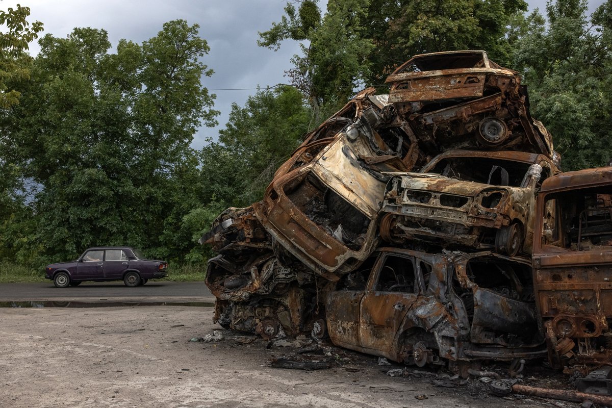 Машина проезжает мимо груды сгоревших автомобилей, уничтоженных во время российской оккупации, в Гостомеле, Украина, 19 июля 2022 года. Фото: Роман Пилипей / EPA-EFE