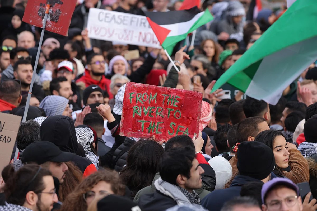 Люди, среди которых один держит плакат с надписью: «От реки до моря», скандируют лозунги под палестинскими флагами во время акции протеста «Свободу Палестине», собравшей тысячи участников 04 ноября 2023 г. в Берлине. Фото: Sean Gallup / Getty Images