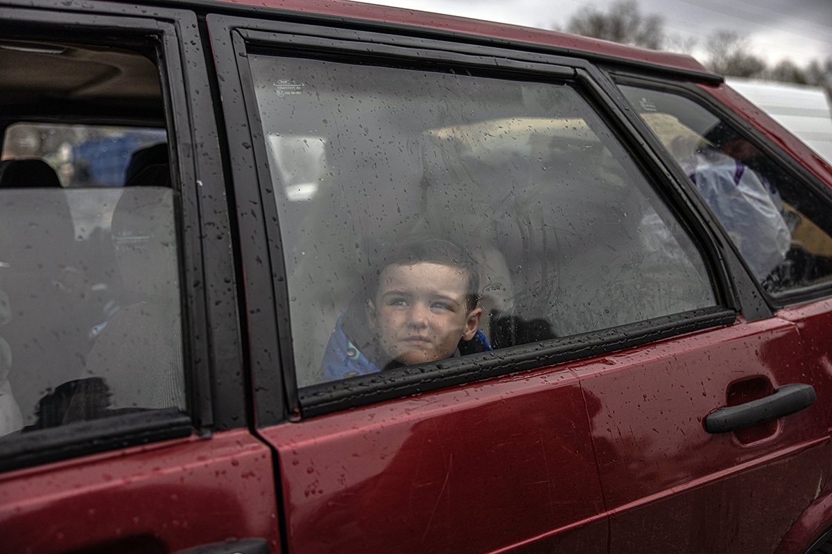 Мальчик за стеклом машины после прибытия из Мелитополя в пункт эвакуации в Запорожье, Украина, 21 апреля 2022 года. Фото: Роман Пилипей/EPA-EFE