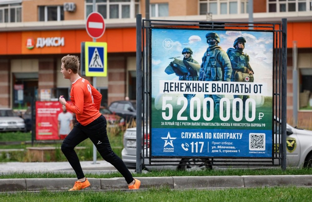 A man jogs past a military recruitment poster in Moscow, August 2024. Photo: EPA-EFE / YURI KOCHETKOV