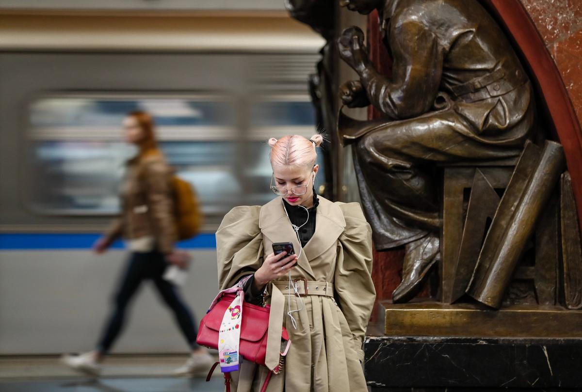 Девушка смотрит в свой телефон в ожидании поезда на станции метро в Москве, Россия, 19 апреля 2023 г. Фото: EPA-EFE/YURI KOCHETKOV