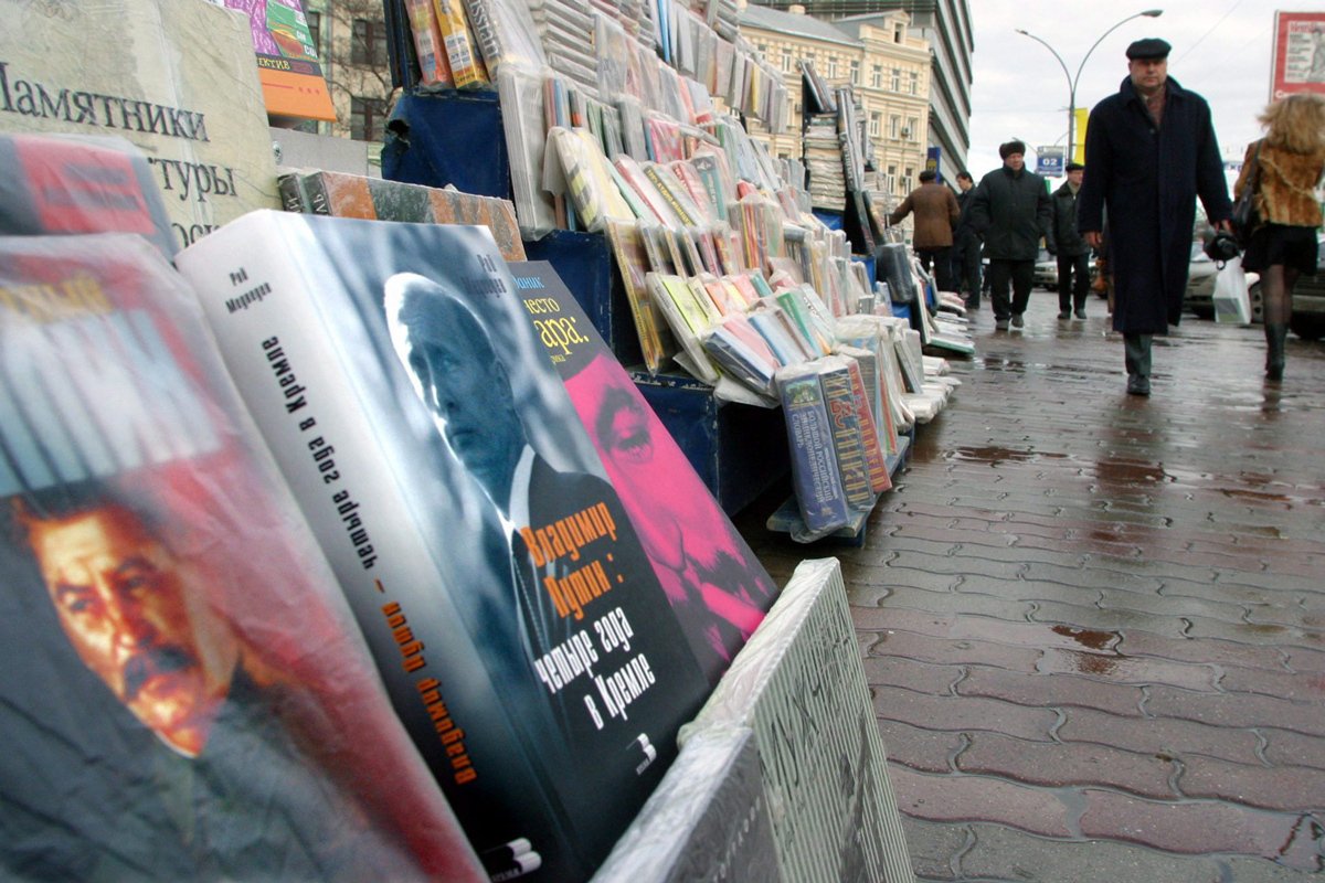 Прохожие проходят мимо книг, на обложках которых изображены Сталин (слева) и президент Владимир Путин (второй слева). Фото: Максим Шипенков / EPA-EFE