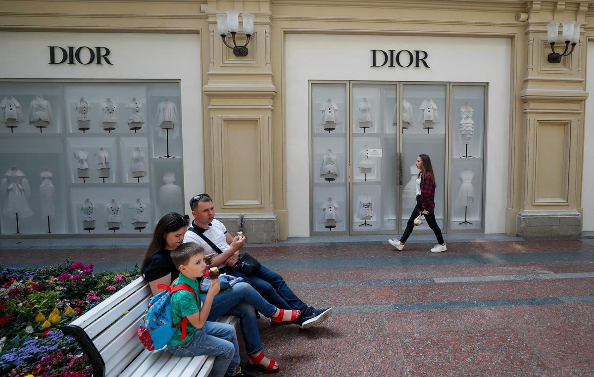 Люди сидят на скамейке перед закрытым магазином Dior в ГУМе в Москве. Фото: Юрий Кочетков / EPA-EFE