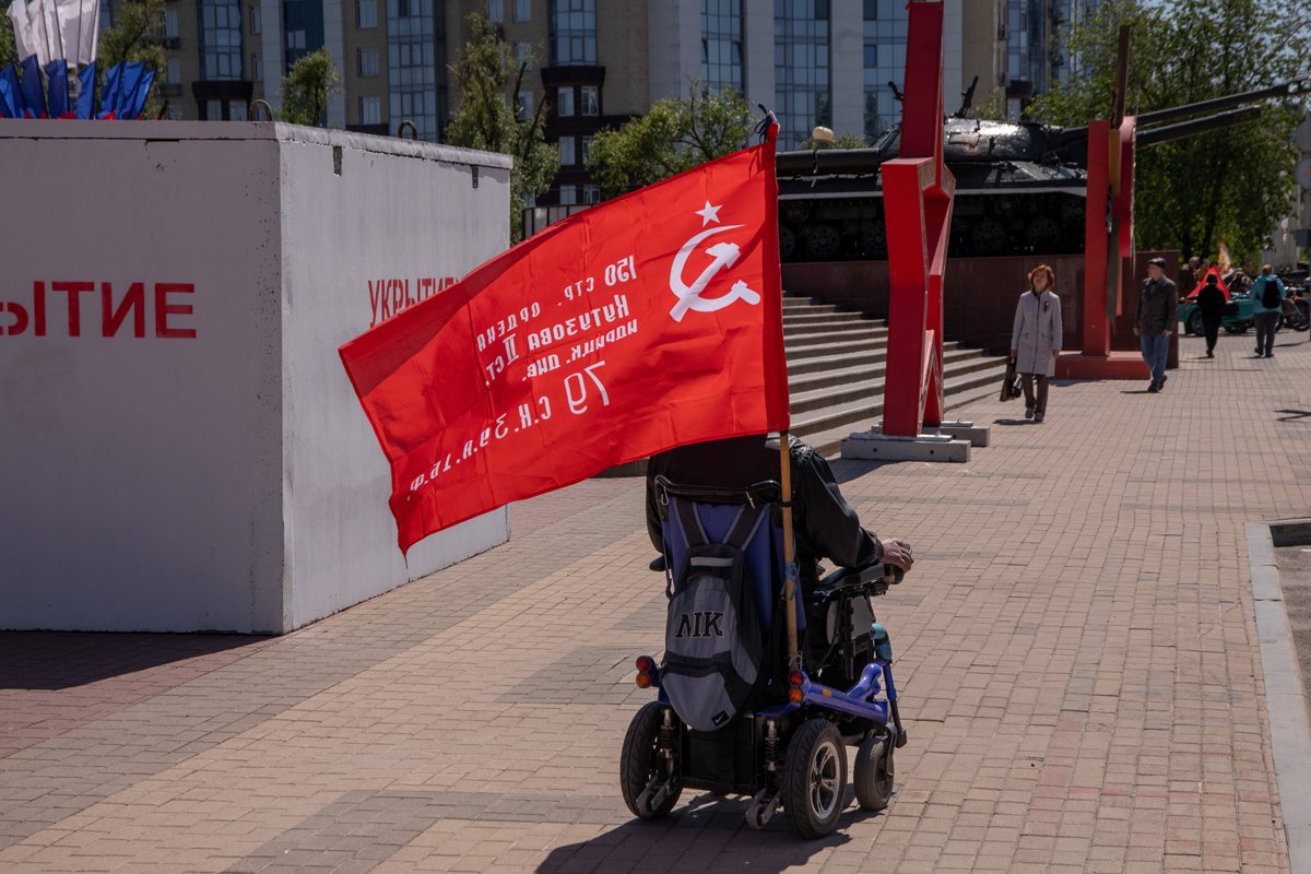 Пенсионер с красным флагом на фоне танка в Белгороде, 9 мая 2024 года. Фото: Александр Каратаев / «Новая газета Европа»