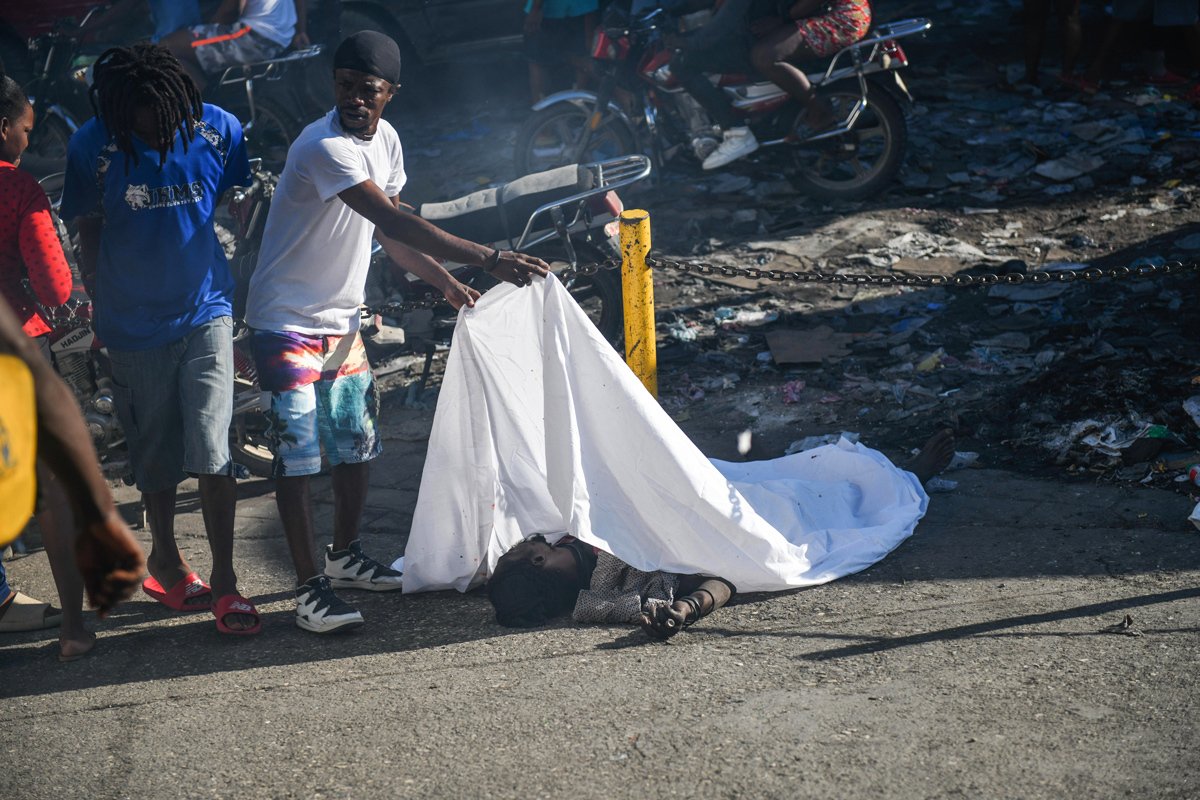 Мужчина накрывает тело человека, лежащего на земле, на одной из улиц Порт-о-Пренса, Гаити, 18 марта 2024 года. Фото: Johnson Sabin / EPA-EFE