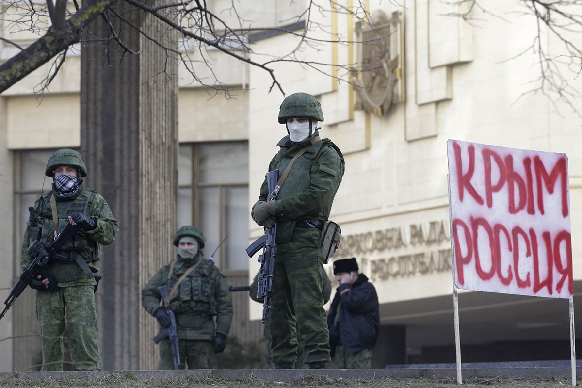 Неопознанные вооруженные люди в военной форме стоят возле плаката «Крым — это Россия» перед зданием парламента автономии в Симферополе, Украина, 1 марта 2014 года. Фото: Максим Шипенков / EPA