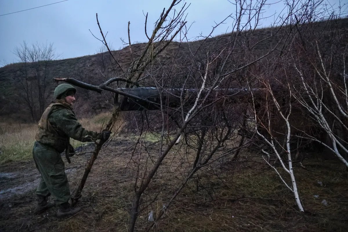 A fighter lays branches over a field gun at a position near Avdiivka, eastern Ukraine. Photo: Alessandro Guerra / EPA-EFE