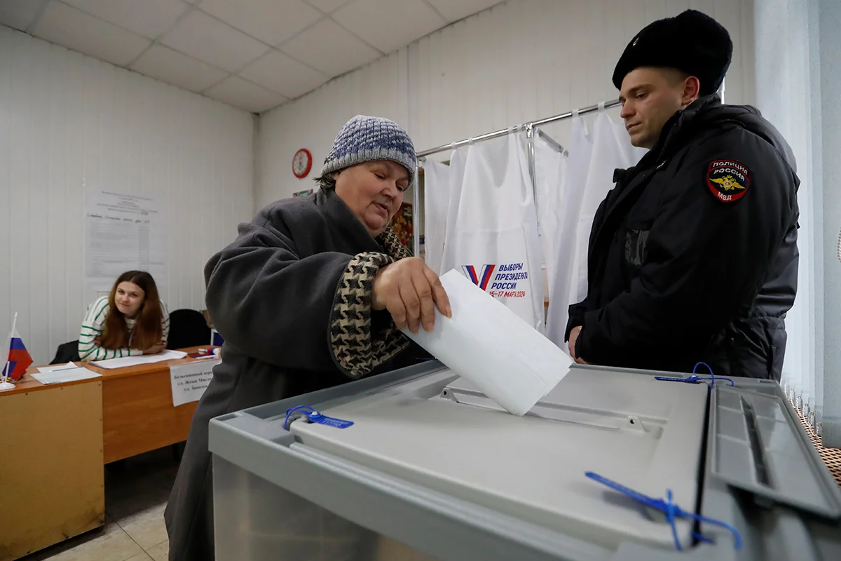 A woman votes at a polling station in the village of Lyuban, Leningrad Region, under the supervision of a police officer, March 16, 2024. Photo: Anatoliy Maltsev / EPA-EFE
