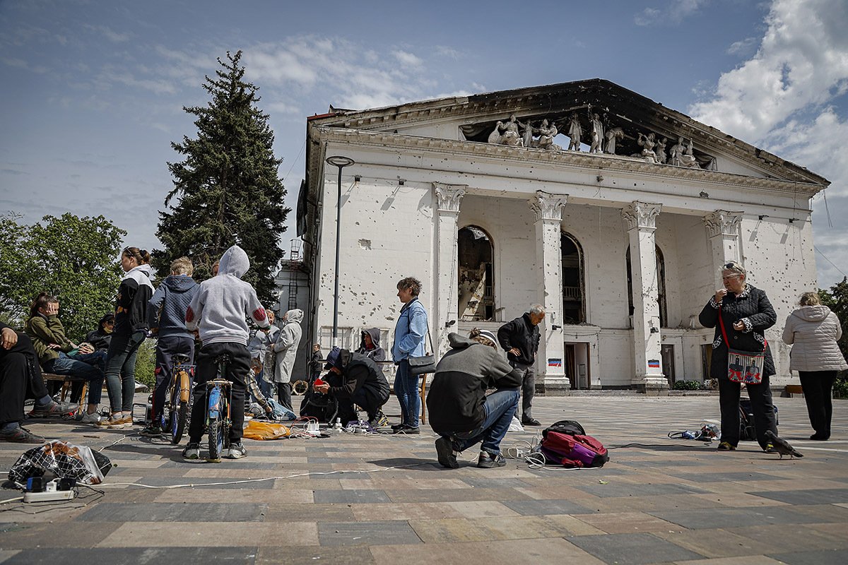 Местные жители заряжают свои мобильные телефоны возле разрушенного драматического театра в Мариуполе, Украина, 21 мая 2022 года. Фото: Alessandro Guerra / EPA-EFE