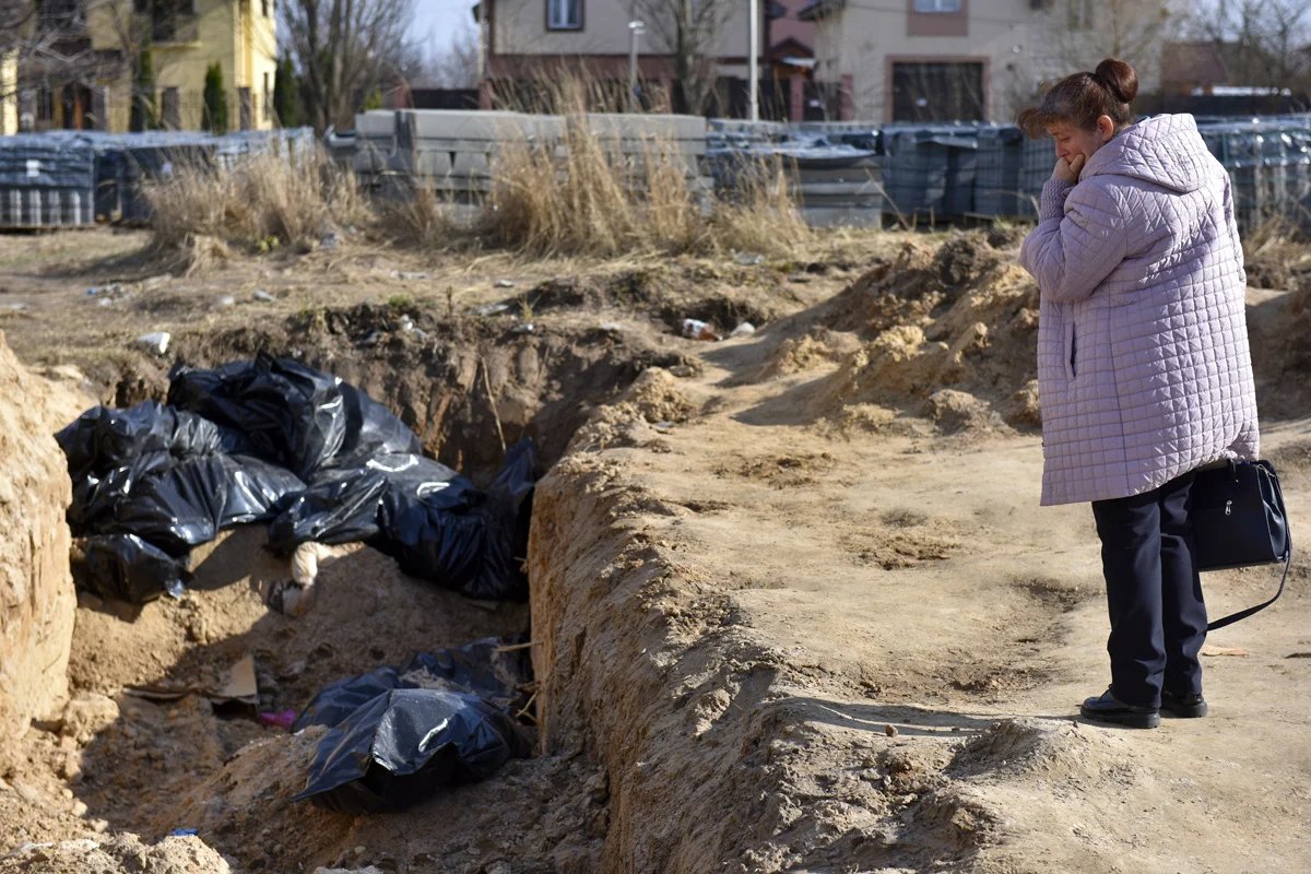 A woman looks down into a mass grave in Bucha, 7 April 2022. Photo: Oleg Petrasiuk / EPA-EFE