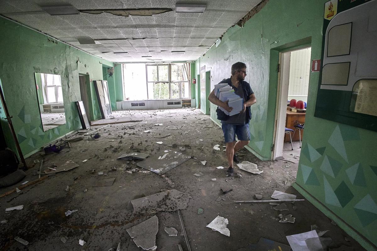 Мужчина несет книги в школе, пострадавшей во время обстрела, в городе Чугуев, Украина, 25 июля 2022 г. Фото: SERGEY KOZLOV / epa.eu