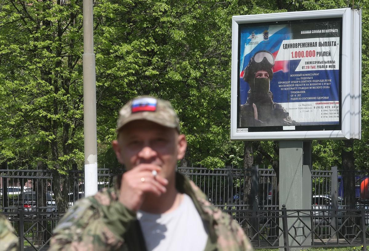 A man in military uniform stands in front of a poster promoting military enlistment in Podolsk, outside Moscow, 17 May 2024. Photo: EPA-EFE / MAXIM SHIPENKOV