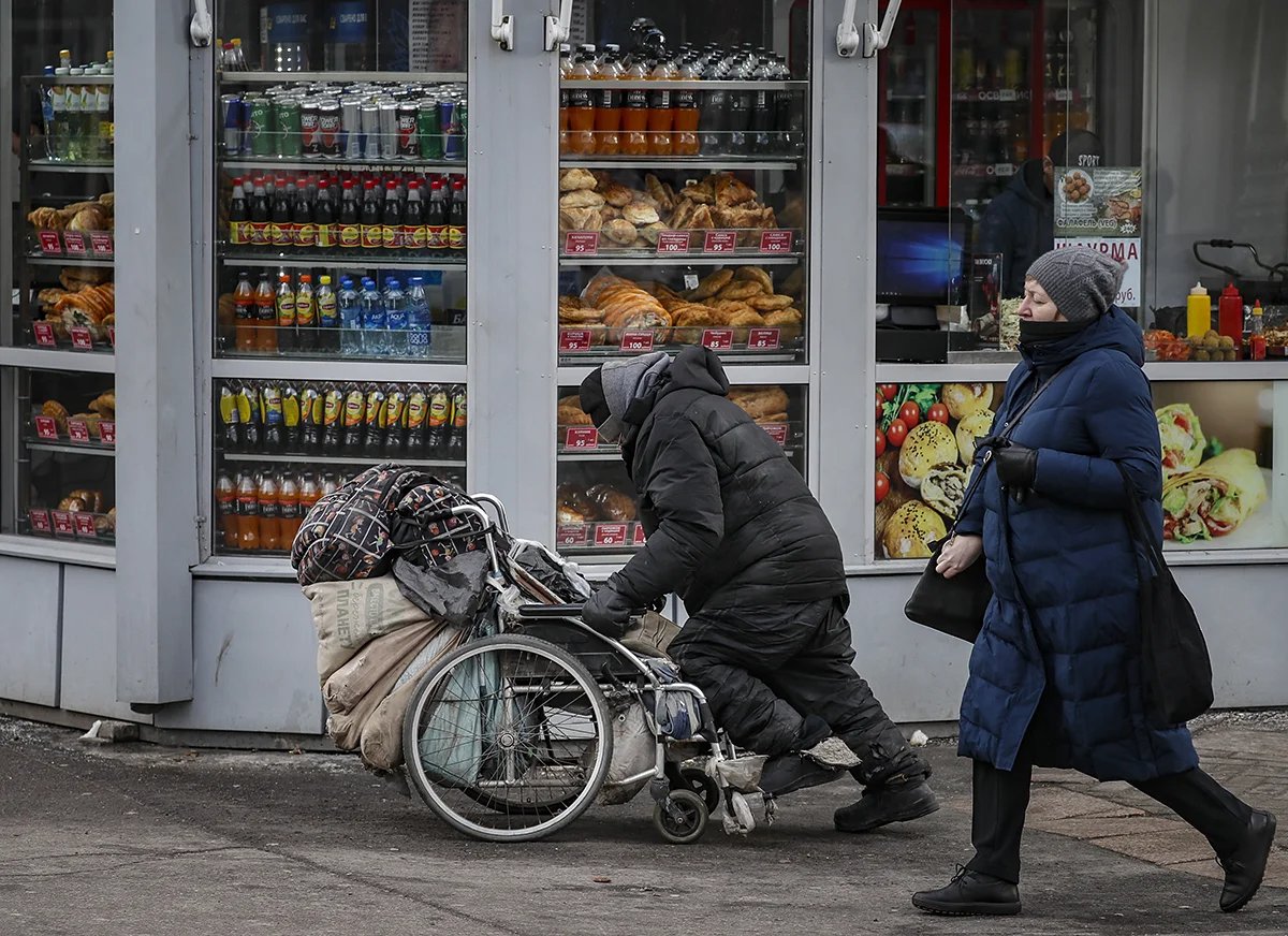 An unhoused man pushes a wheelchair with his belongings past a shop window in Moscow. Photo: Yury Kochetkov / EPA-EFE