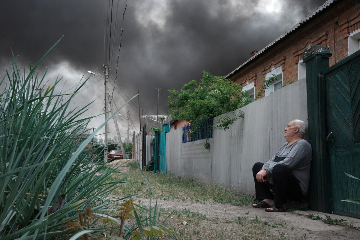 A man sits outside his home as clouds of smoke rise in the distance above Ukraine’s Kharkiv region following the start of the Russian offensive. Photo: EPA-EFE/GEORGE IVANCHENKO