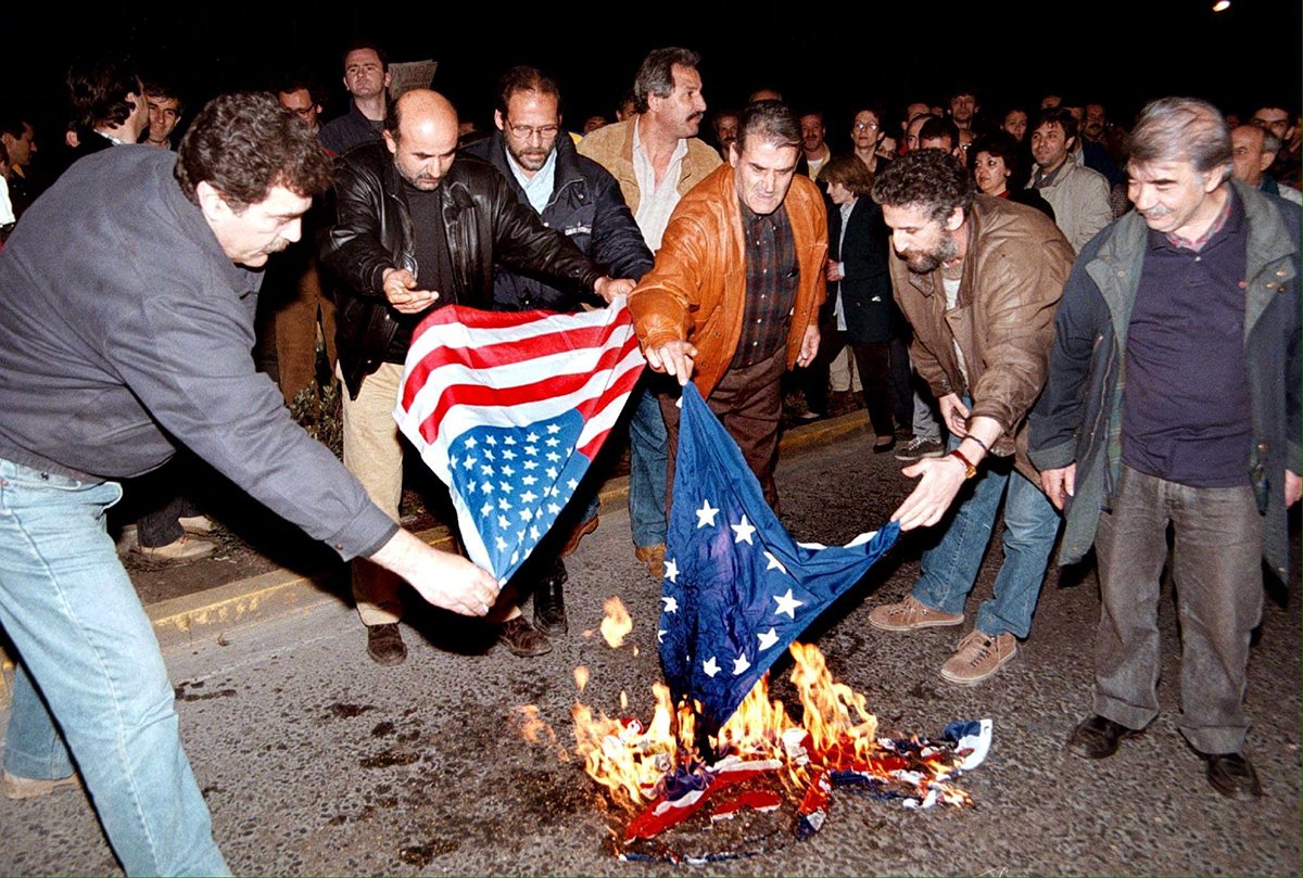 Протестующие сжигают флаги США и Европейского союза перед посольством США в Афинах во время акции протеста против авиаударов НАТО по Югославии, 26 марта 1999 года. Фото: Pantelis Saitas / EPA/ANA