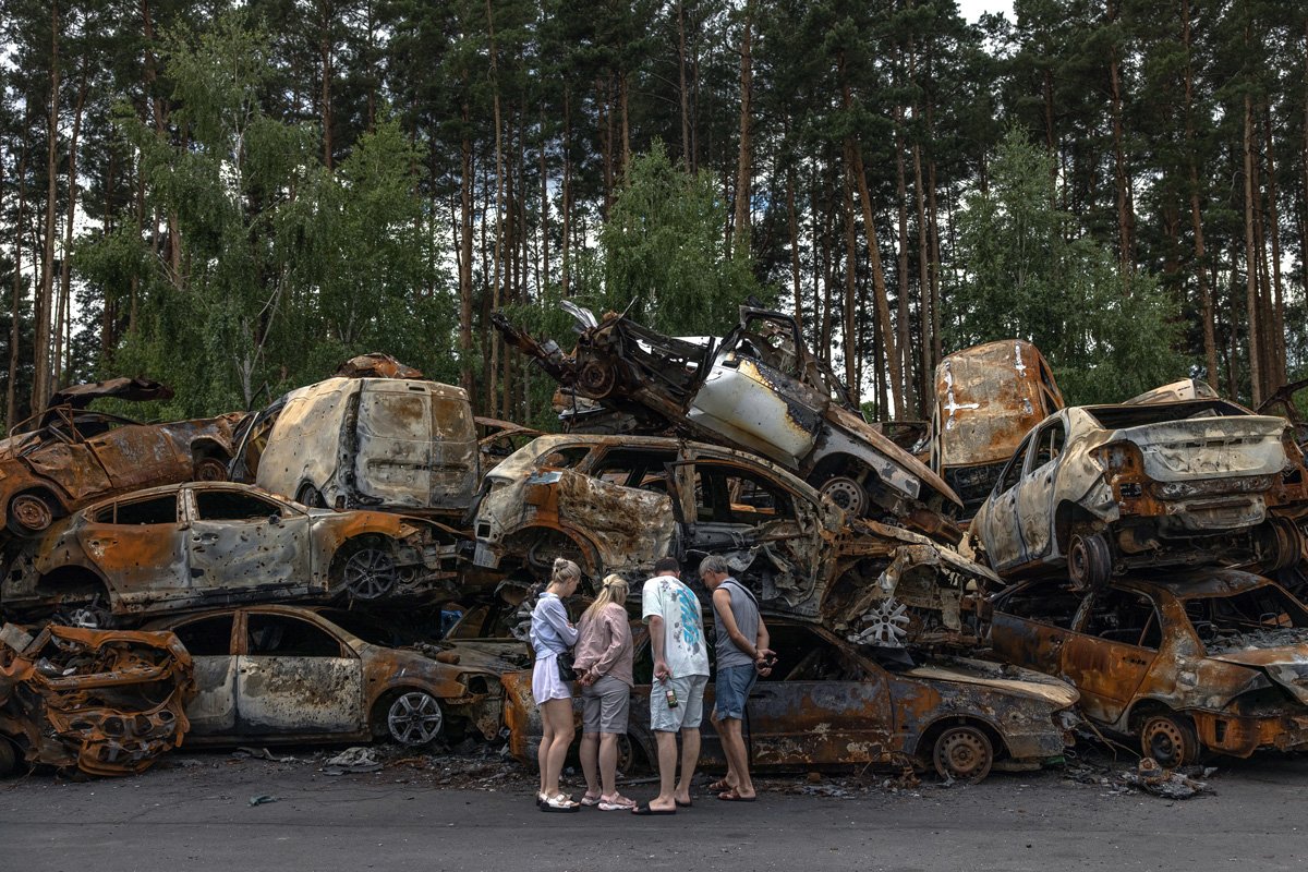 Люди смотрят на груды сгоревших автомобилей, уничтоженных во время российских атак в Ирпене, 16 июня 2022 года. Фото: Роман Пилипей / EPA-EFE