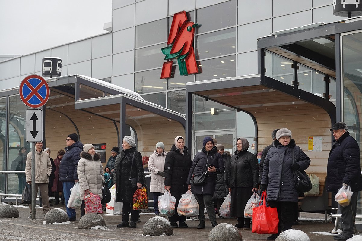 Люди у автобусной остановки перед магазином французской сети Auchan в торговом центре Мега, Москва, Россия, 16 февраля 2023. Фото: Максим Шипенков / EPA-EFE