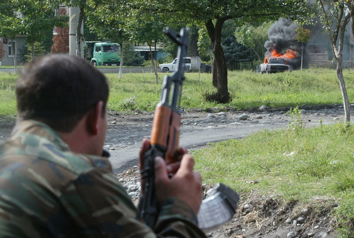 Солдат смотрит на автомобиль, сгоревший в результате обстрела из гранатомета здания школы, захваченного группой террористов, Беслан, четверг, 2 сентября 2004 года. Фото: Юрий Кочетков/EPA