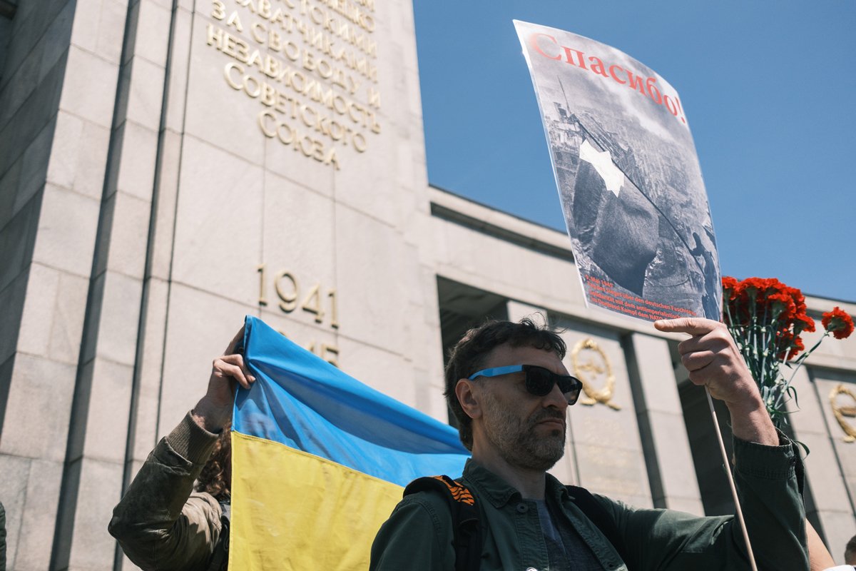 Посетители мемориала перекрывают украинский флаг плакатами. Фото: Даниил Маштаков