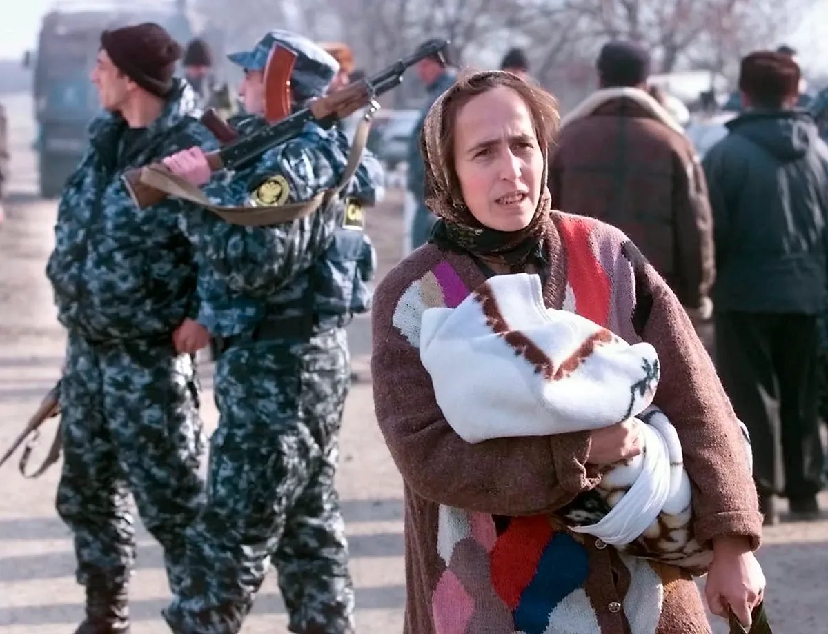 Chechen woman carries her child, passing by Russian soldiers on her way to the refugees camp on the Chechen-Ingush border, 1999. Photo: EPA / YURI KOCHETKOV