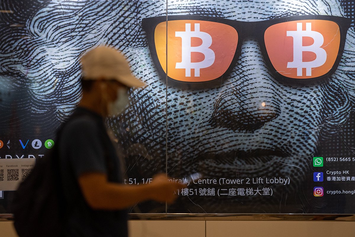Мужчина идет мимо рекламного плаката биткоинов и криптовалют в Гонконге, Китай. Фото: Jerome Favre / EPA-EFE
