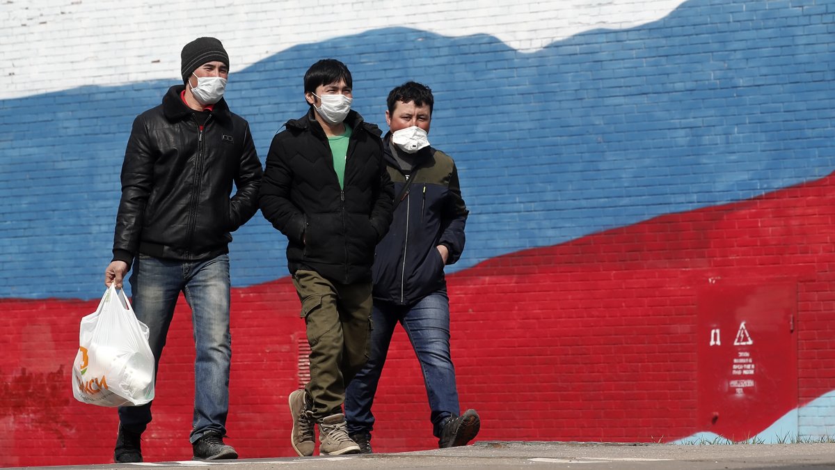 Мигранты из Цетральной Азии на фоне стены в цвете российского флага в Москве, 13 апреля 2020 года. Фото: Максим Шипенков / EPA-EFE