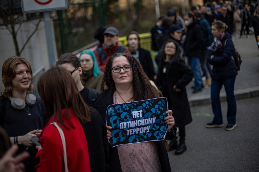 A woman holds a placard that reads “No to Putin’s terror” as Russian nationals wait in line to vote in the presidential elections at the Russian embassy in Prague, Czechia, 15 March 2024. Photo: EPA-EFE/MARTIN DIVISEK